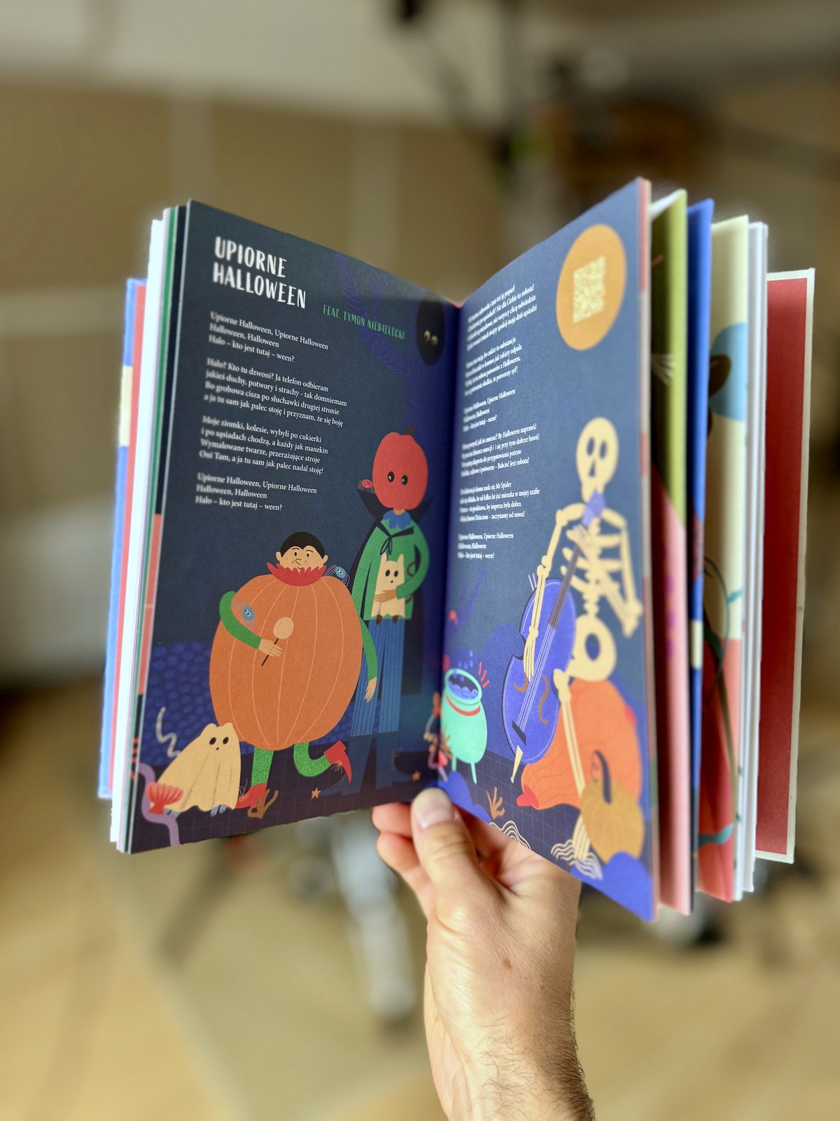 Rozkładówka książki „Niegłupie Piosenki” z piosenką „Upiorne Halloween” — widoczny kod QR